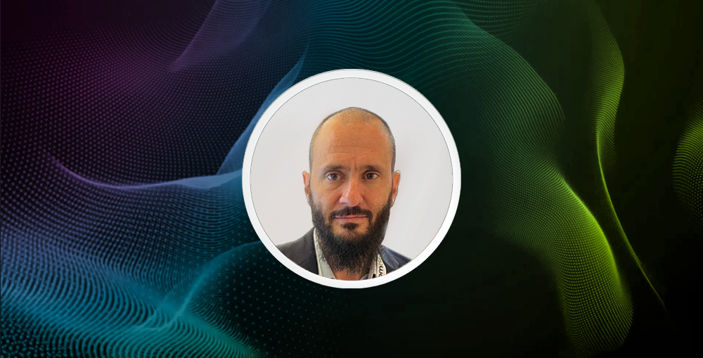 Ali Karaman’s headshot in a white circular frame against a colourful digital wave background.